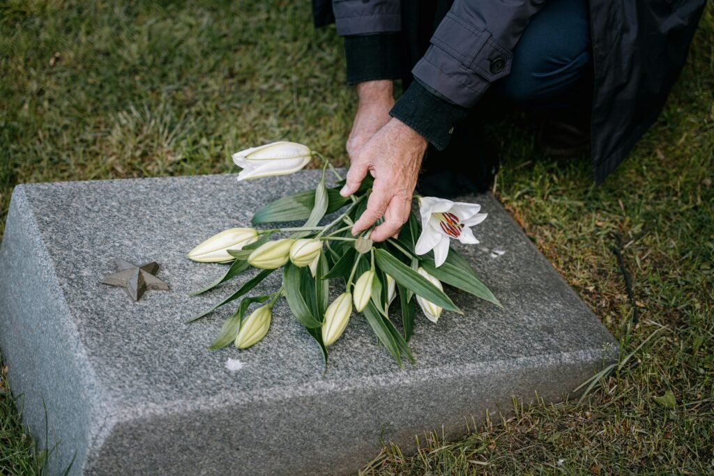 A person placing white lilies on a tombstone in memory of a loved one.